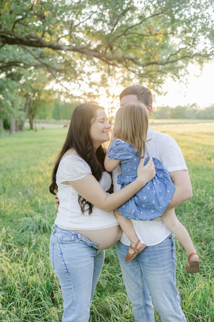 A pregnant couple snuggles their toddler in an open field during golden hour maternity family photos in Afton, MN.